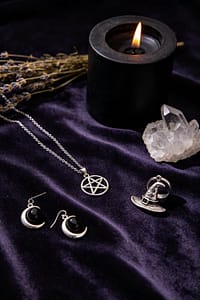 Witch jewelry collection with pentagram necklace, crescent moon earrings, black onyx ring and witch hat pendant on dark velvet